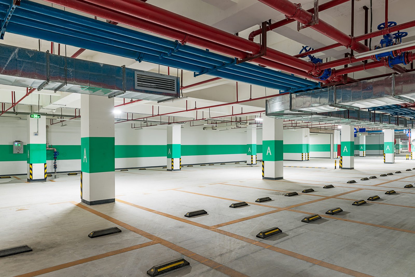 Grade de colunas e corredor de acesso sob linhas MEP vermelhas/azuis em um subsolo de estacionamento