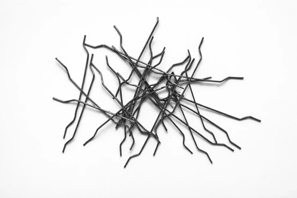 Hooked end steel fiber scattered on a light gray background for concrete reinforcement