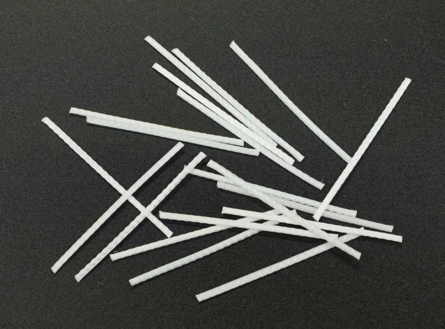 Long embossed polypropylene macrofibers sit beside fresh concrete and a concrete slab sample.